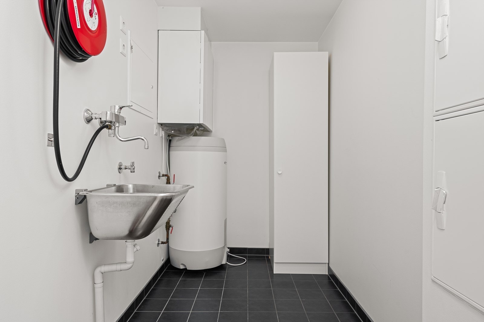 Praktisk vaskerom/bod med flislagt gulv, utslagsvask og opplegg for vaskemaskin. Galleribilde