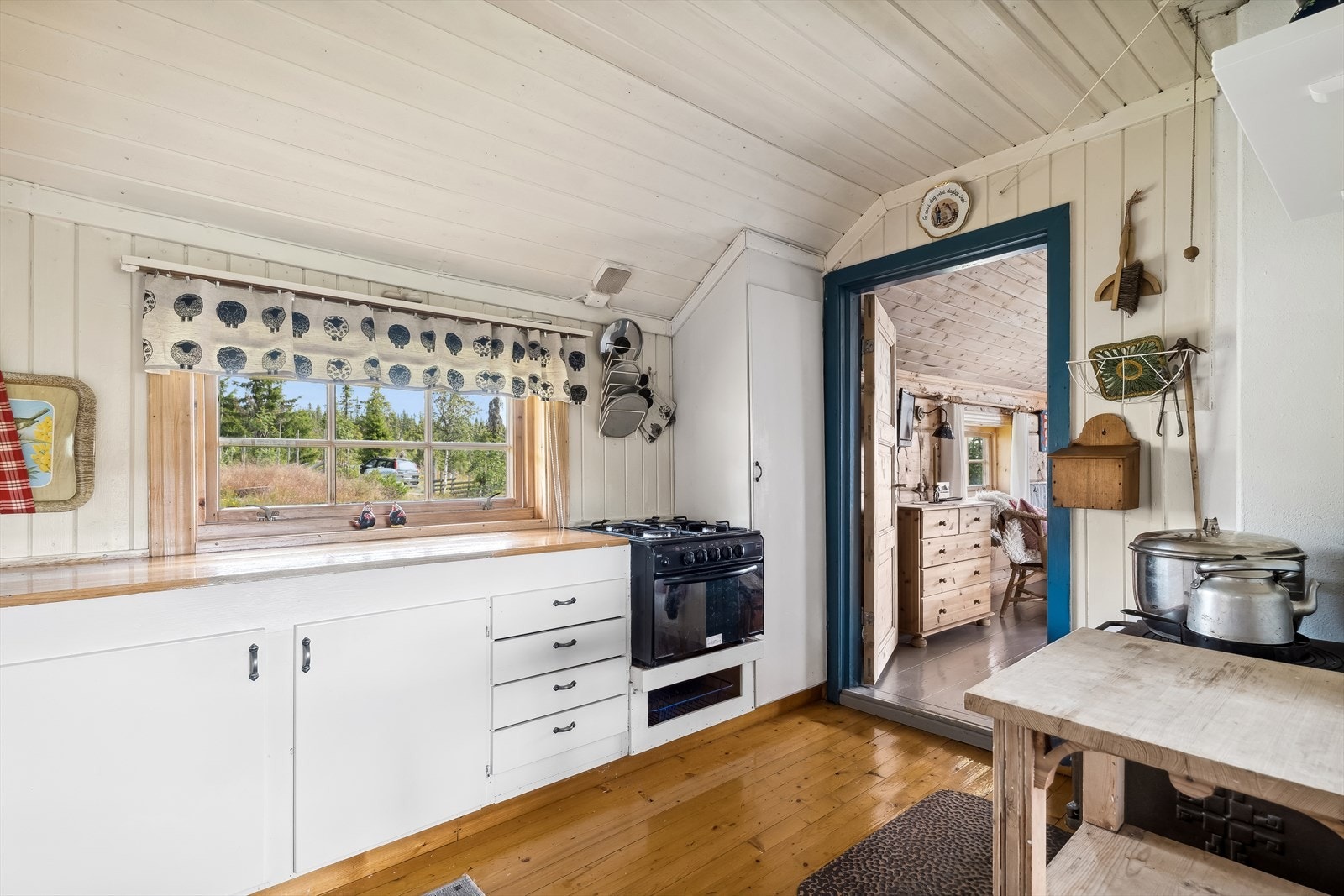Kjøkkenet har hvitmalt panel på veggene og tregulv. Enkel kjøkkeninnredning med slette fronter og heltre benkeplater montert på ytterveggen. Galleribilde