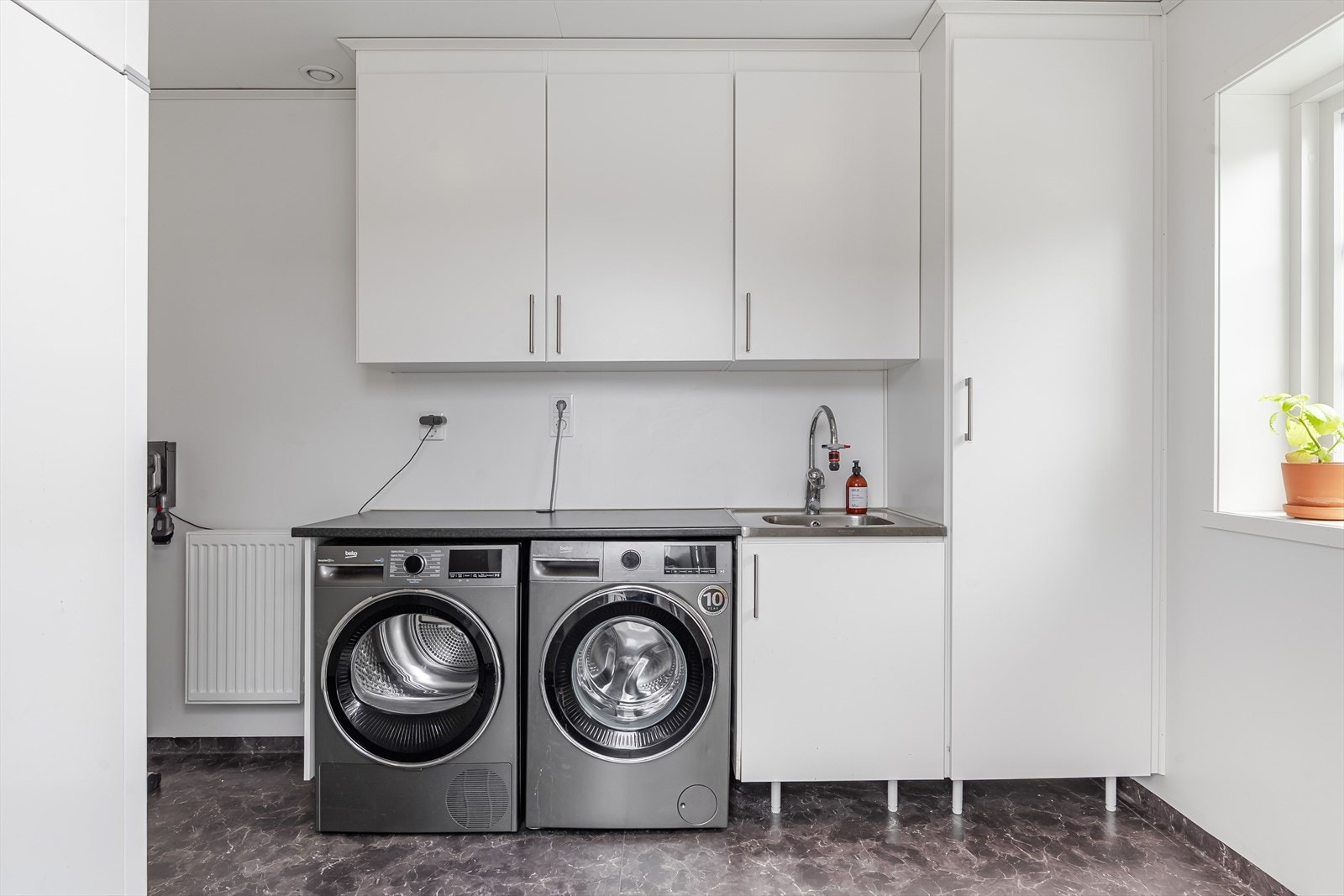 Fra kjøkkenet er det adkomst til et lyst vaskerom av god størrelse. Lys innredning med laminert benkeplate og nedfelt kum. Praktisk med plass og opplegg for både vaskemaskin og tørketrommel under benkeplaten. Galleribilde