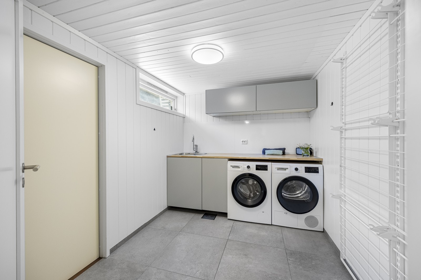 På innsiden av badet ligger vaskerommet. Her er det egen dør ut, praktisk om man skal henge uyt klesvasken eller om noen kommer skitne hjem. Diverse innredning og skap, smat benkeplate. Vegghengte tørkestativ på veggen. Galleribilde