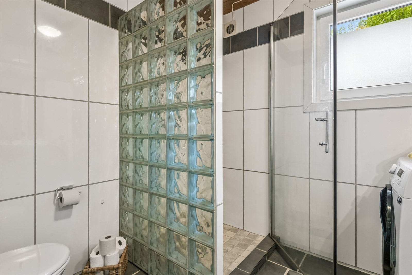 Dusjnisje avskjermet med glassbyggerstein og glassdør. Badet har også en elektrisk styrt vifte. Galleribilde