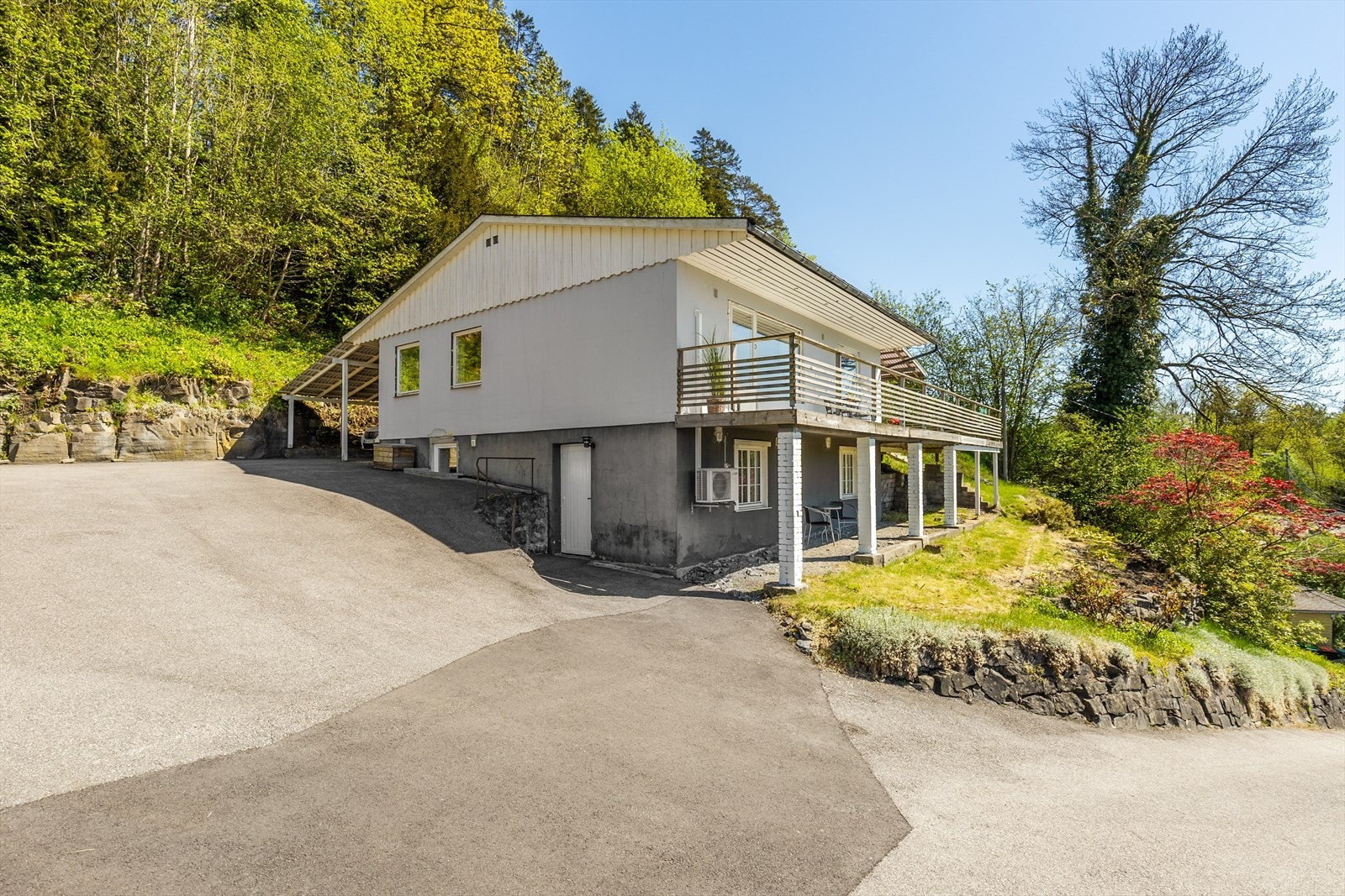 Adkomst og gårdsplass er i hovedsak asfaltert. Boligen har en tilliggende carport, og på tomten er det oppført en frittstående garasje nede ved veien. Galleribilde