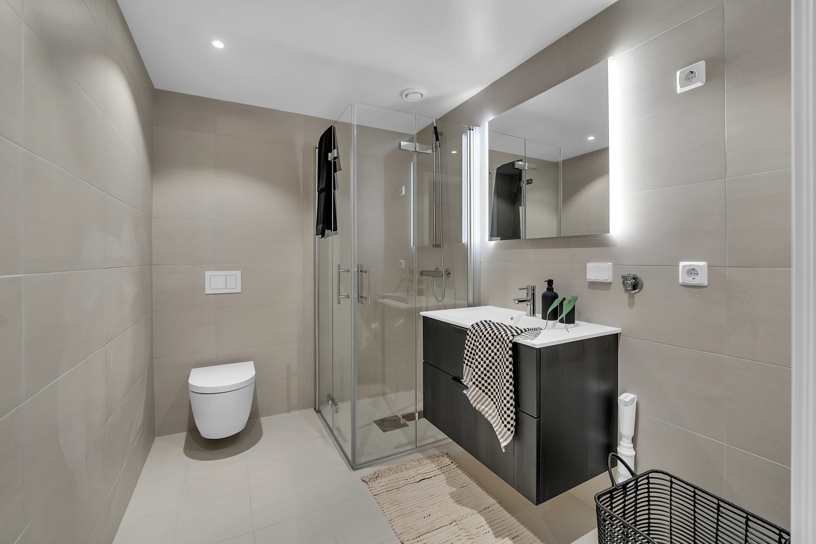 Badet har sandfargede fliser, downlights i taket og innredning fra HTH. Servantskap i sort trelook. Speil med integrert LED-lys. Dusjen har herdet glassvegger som kan slås inn mot vegg. Det er opplegg for vaskemaskin og tørketrommel Galleribilde