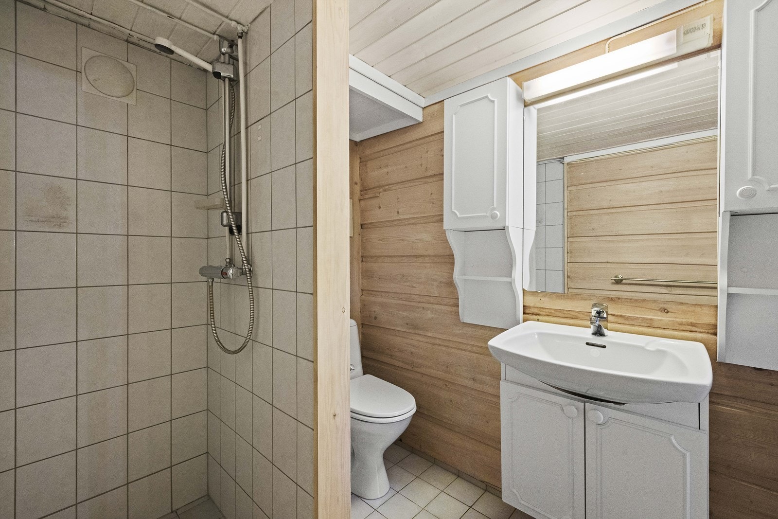 Bad i kjeller har panel på vegger og flis på gulv, med varmekabler Galleribilde