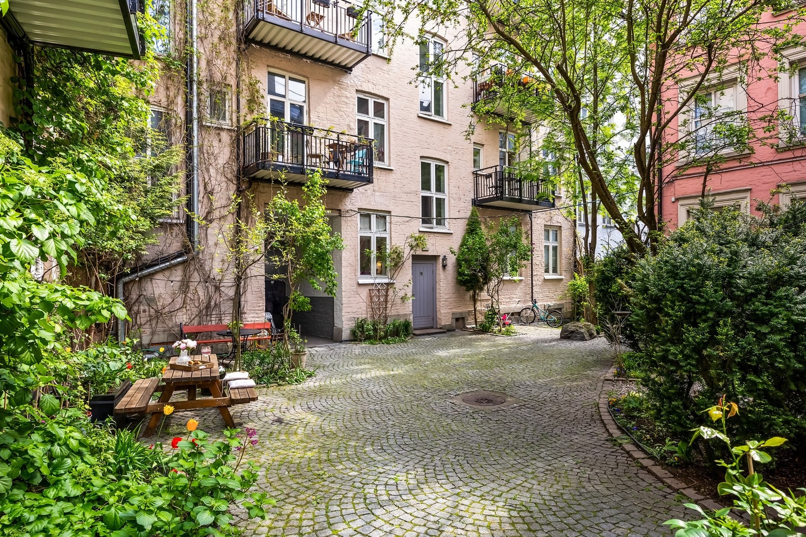 Brosteins belagt bakgård med parkmessig opparbeidet bakhage med plenarealer, sittegruppe under pergola, trær og beplantninger. Galleribilde
