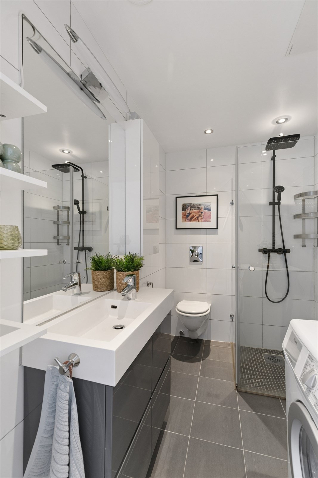 Badet består av veggmontert toalett med skjult sisterne, hjørnedusj med innfellbare glassdører samt servant med tilhørende skuffeinnredning. Galleribilde