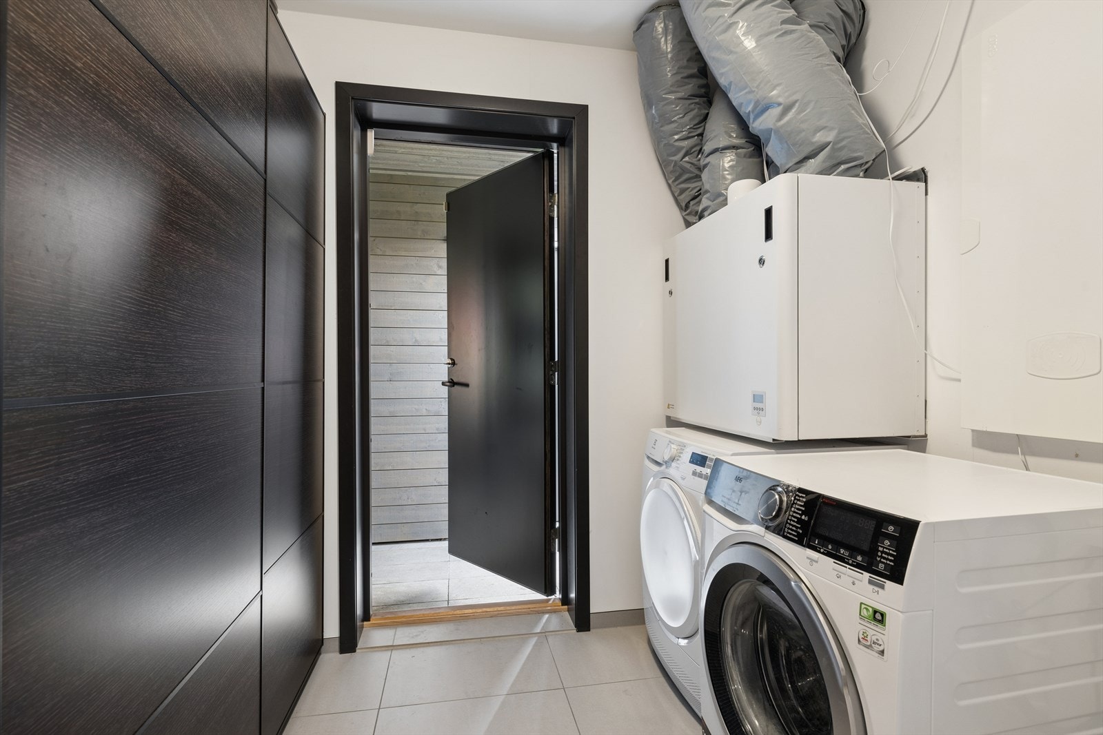 Separat vaskerom med flislagt gulv, opplegg for vaskemaskin og boligens balanserte ventilasjonsanlegg. Egen inngang fra carport og videre inn i boligen. Galleribilde