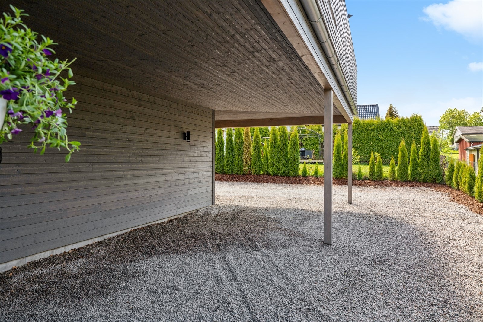 Romslig carport og stor, gruslagt gårdsplass med flere biloppstillingsplasser. Galleribilde