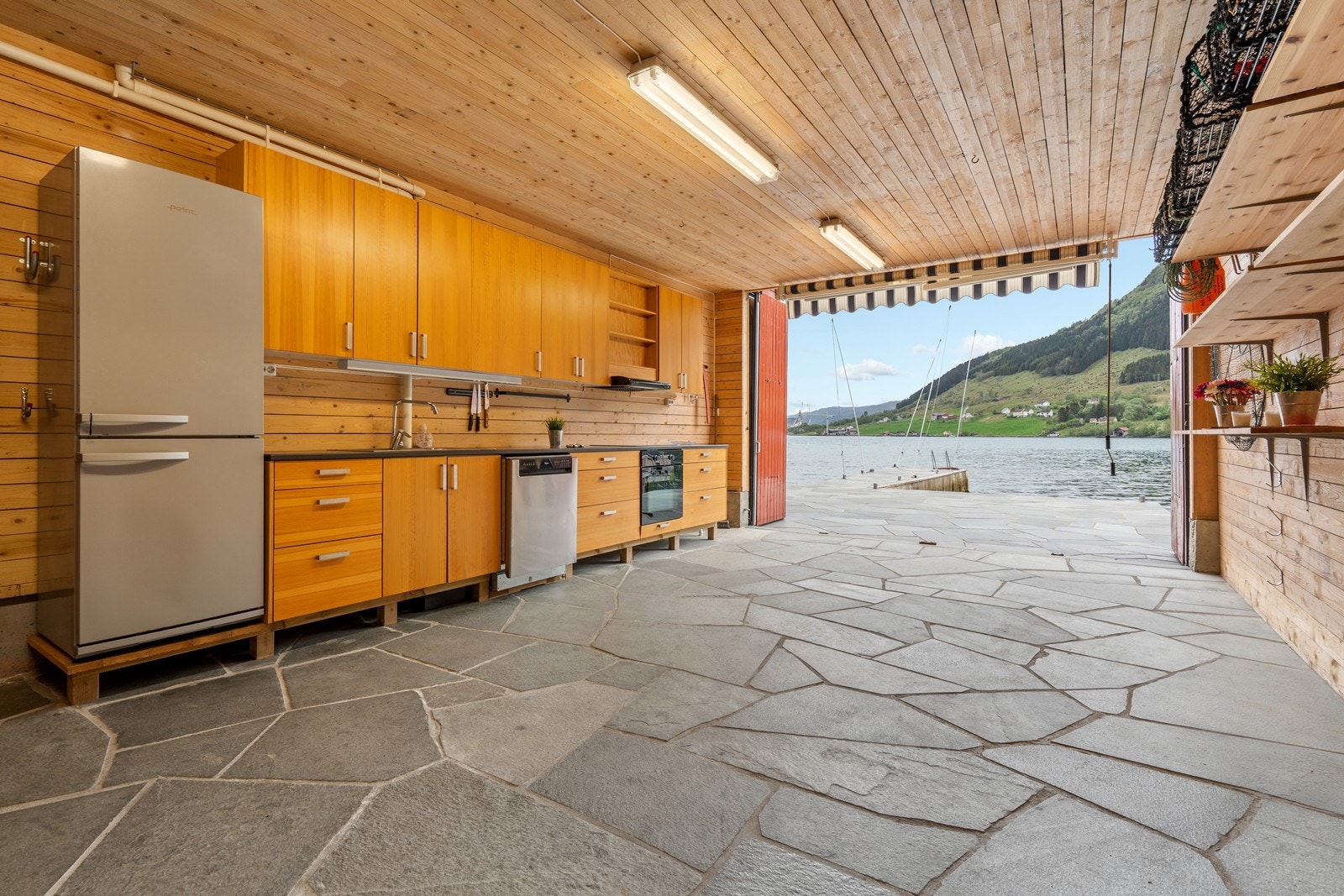Kjøkkeninnredning med lang benkeplate, nedfelt vask, kjøleskap, oppvaskmaskin, stekeovn og induksjon koketopp. Galleribilde