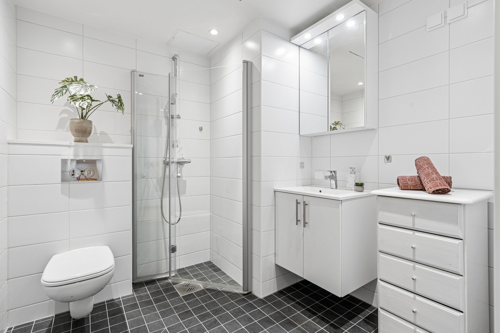 Badet har mørke gulvfliser i kontrast til de lyse veggflisene. Galleribilde