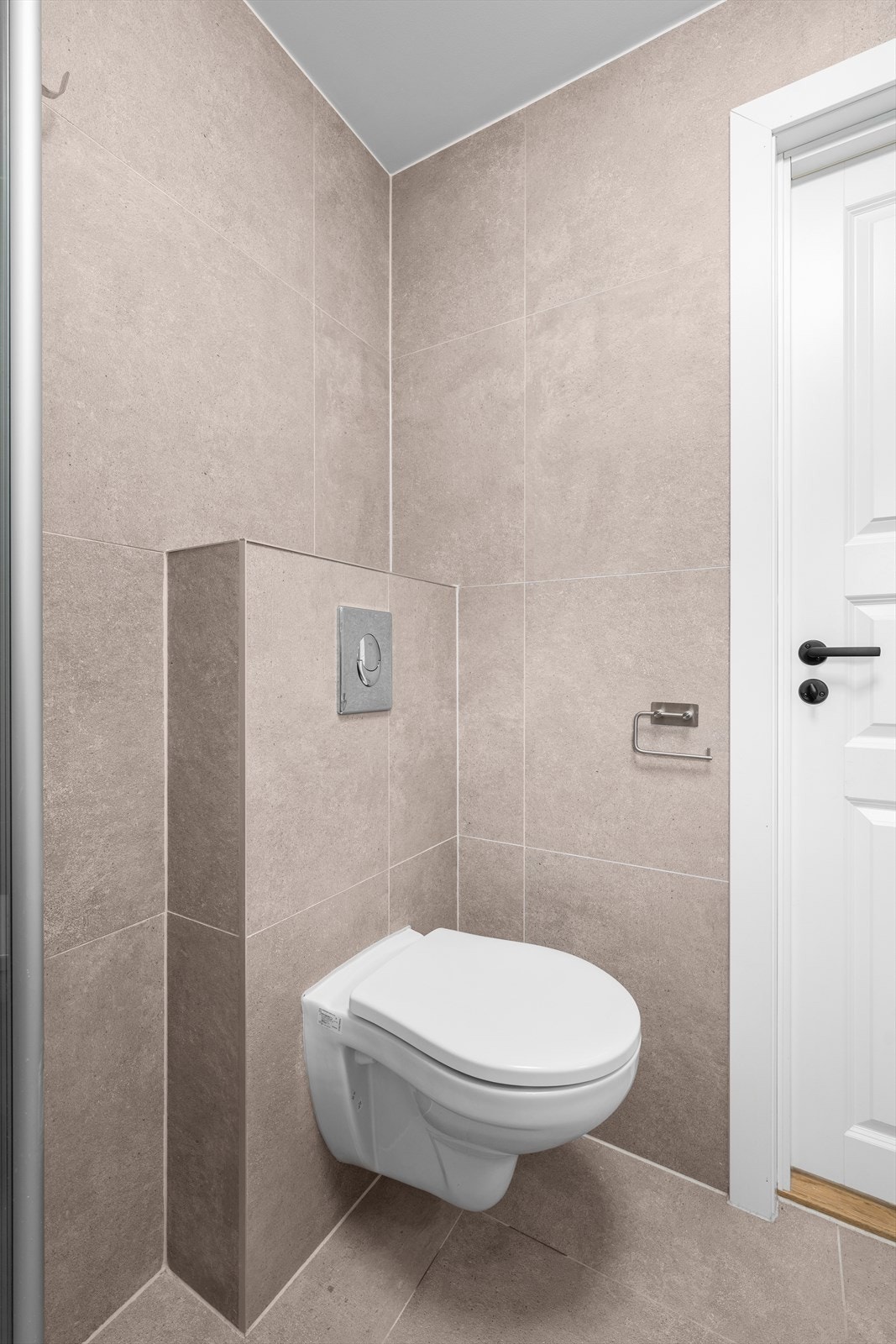 Detalj fra badet som viser det vegghengte toalettet og flislagte overflater. Galleribilde