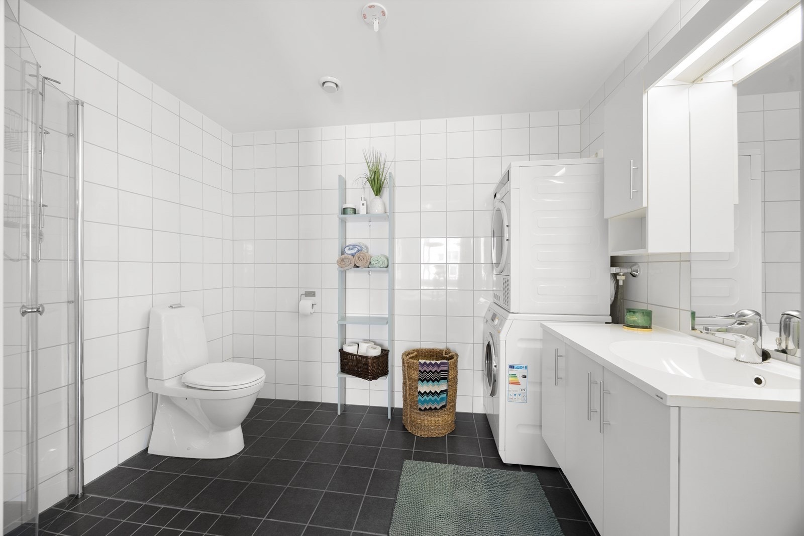 Badet er flislagt på gulv og vegger, og er innredet med servant med dusjhjørne, toalett og innredning. Det er opplegg for vaskemaskin og tørketrommel. Galleribilde