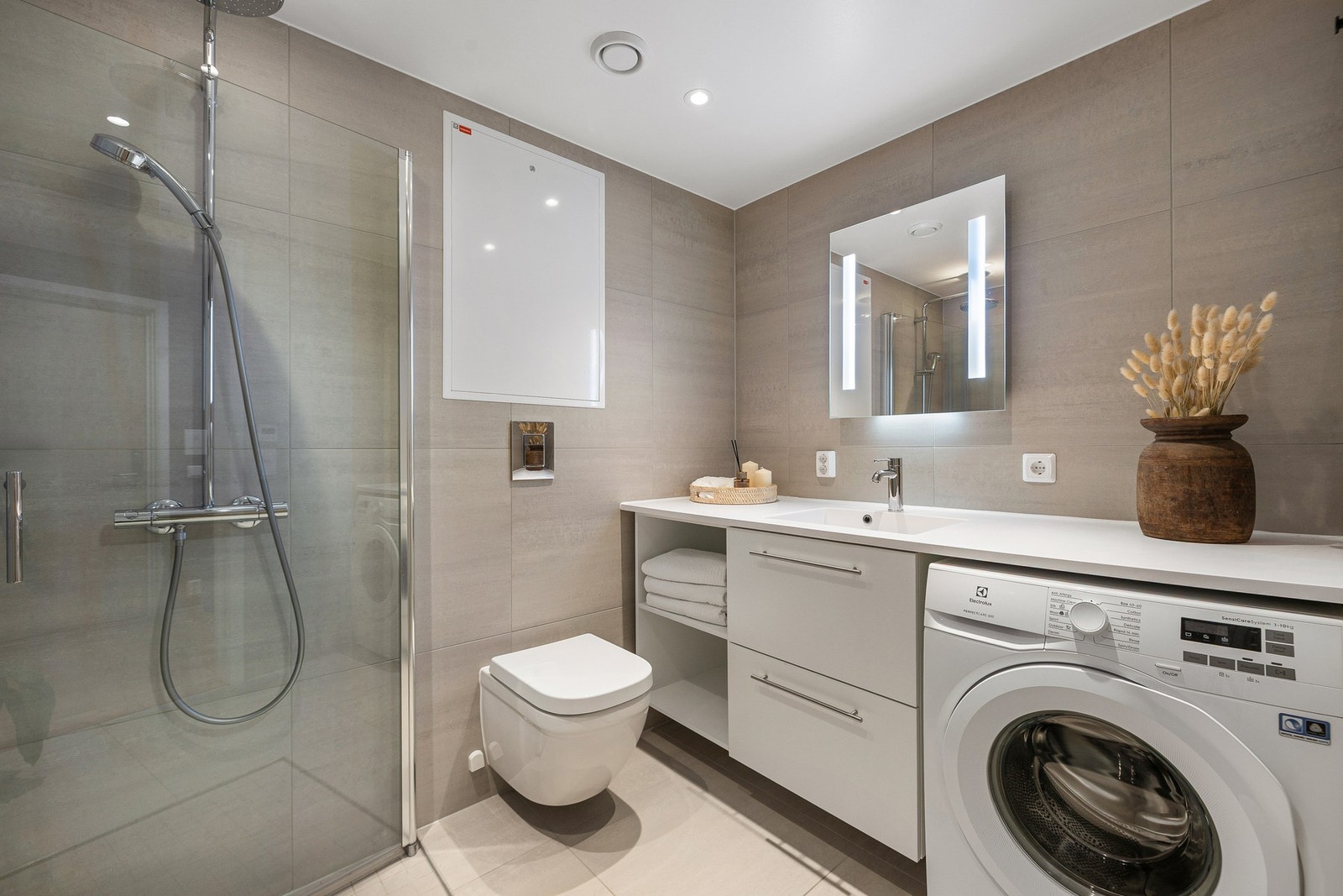 Moderne flislagt bad med eksklusive 60x60-fliser. Badet er utstyrt med dusjhjørne, vegghengt wc, innredning med både hyller og skuffer, samt opplegg for vaskemaskin. Galleribilde