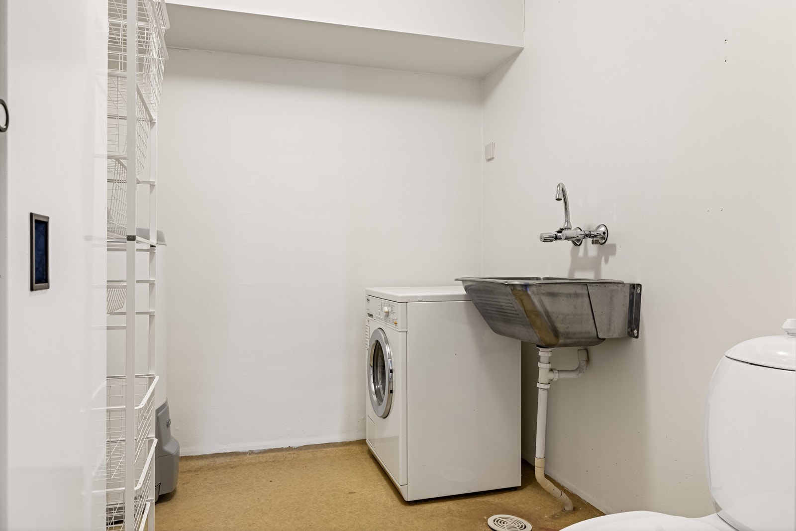 Separat vaskerom med vinyl på gulv, utstyrt med stålkum og opplegg for vaskemaskin. Galleribilde