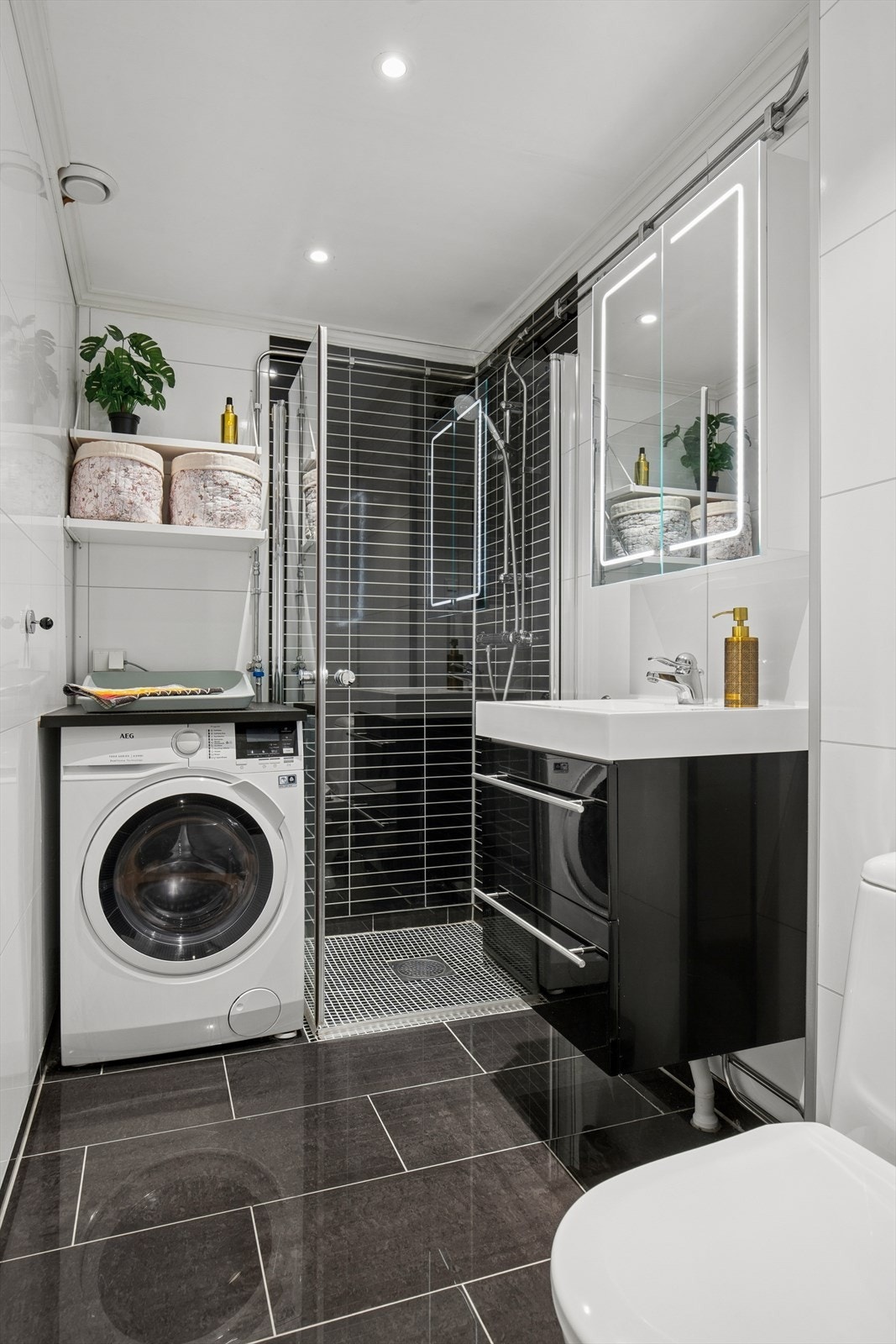Badet fremstår som praktisk og funksjonelt med vegger kledd i baderomsplater, flislagt gulv med behagelige elektriske varmekabler og himling med malte plater. Det er innredet med nedfelt servant, dusj med glassvegger, toalett samt Galleribilde