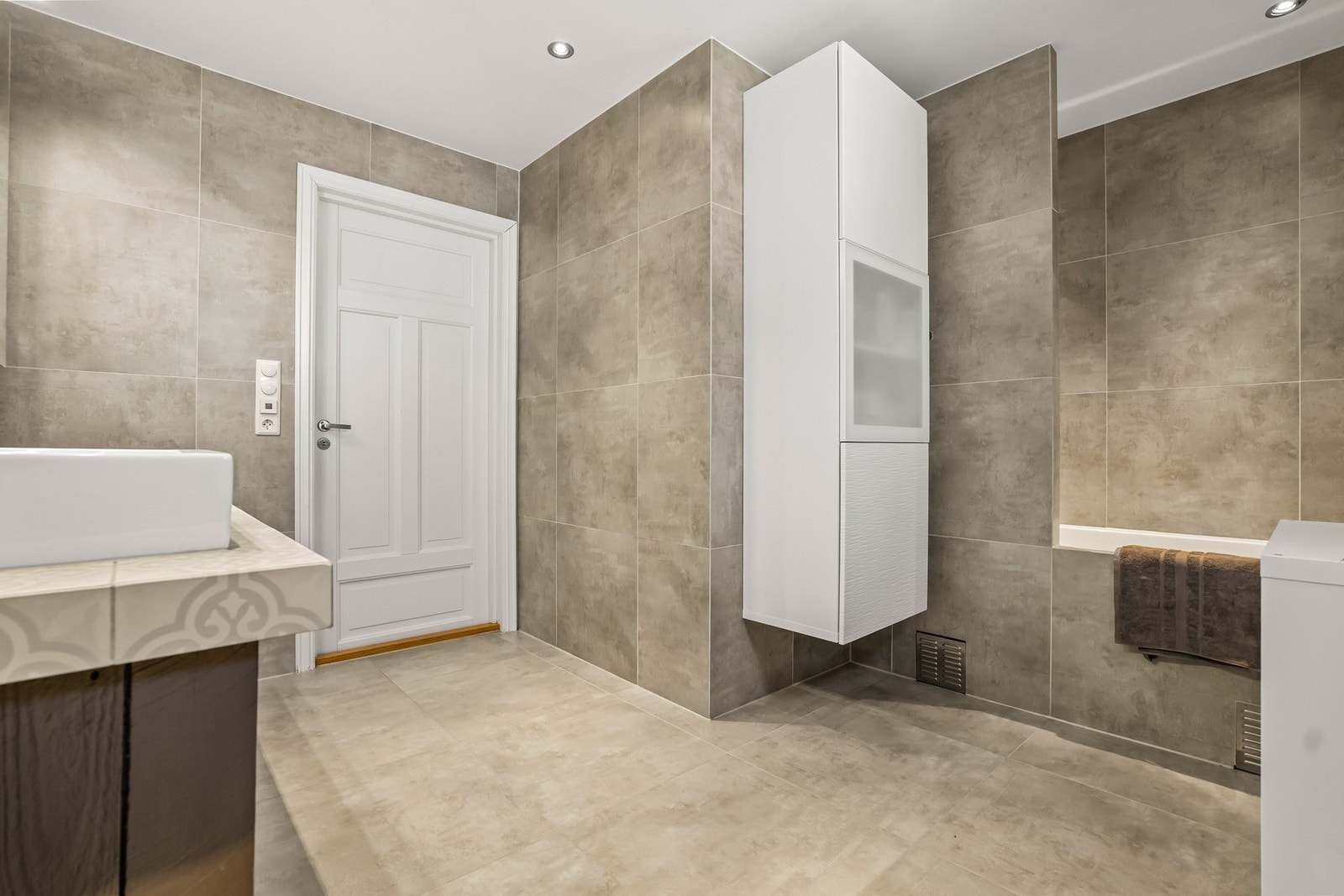 Badet er også utsyrt med dusj i badekar. Den nøytrale fargepaletten gir rommet et tidløst preg, mens varmekabler bidrar til ekstra komfort i hverdagen. Galleribilde