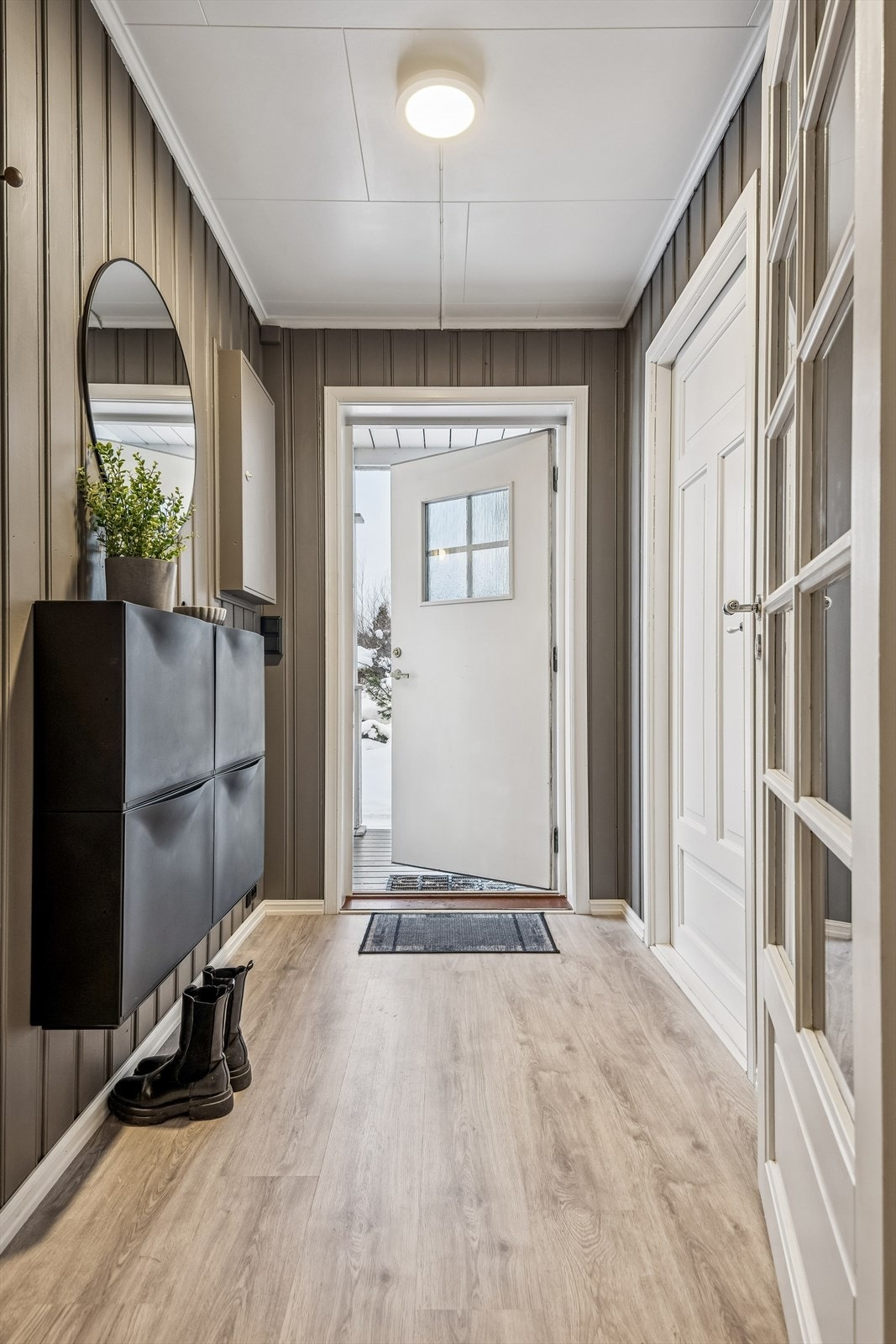 En innbydende entré med laminatgulv fra 2023 og vegger med malt trepanel. Galleribilde