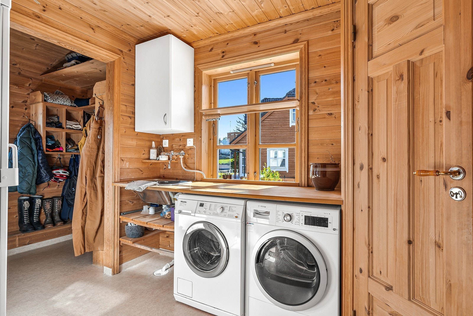 Like ved ligger et romslig og praktisk vaskerom med vinylbelegg på gulv, panel på vegger samt opplegg for vaskemaskin, tørketrommel og utslagsvask. Galleribilde