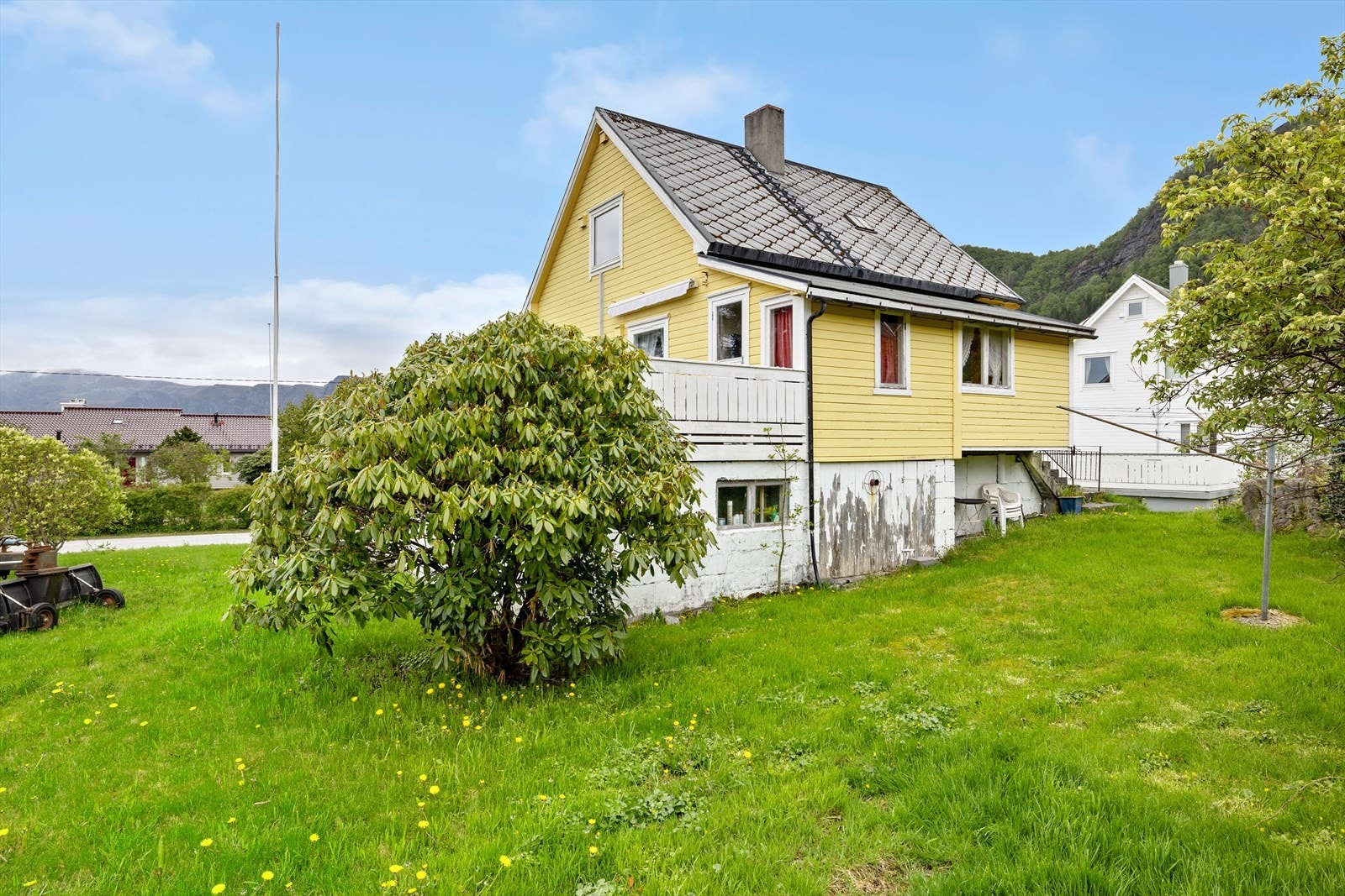 Eit sjarmerande og grønt hageområde med plenareale, prydbusker og vintergrøn beplantning - flatt og fint, perfekt for både trampoline, ballspel og leik. Galleribilde