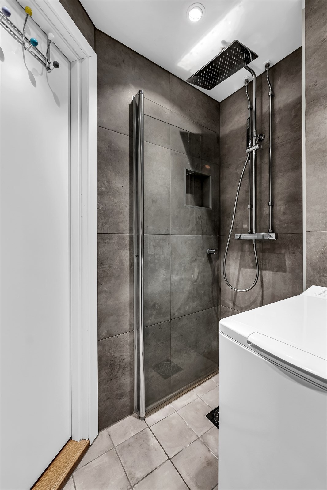Badet er utstyrt med innredning med nedfelt servant, veggmontert toalett, dusjvegger i glass samt opplegg for vaskemaskin Galleribilde