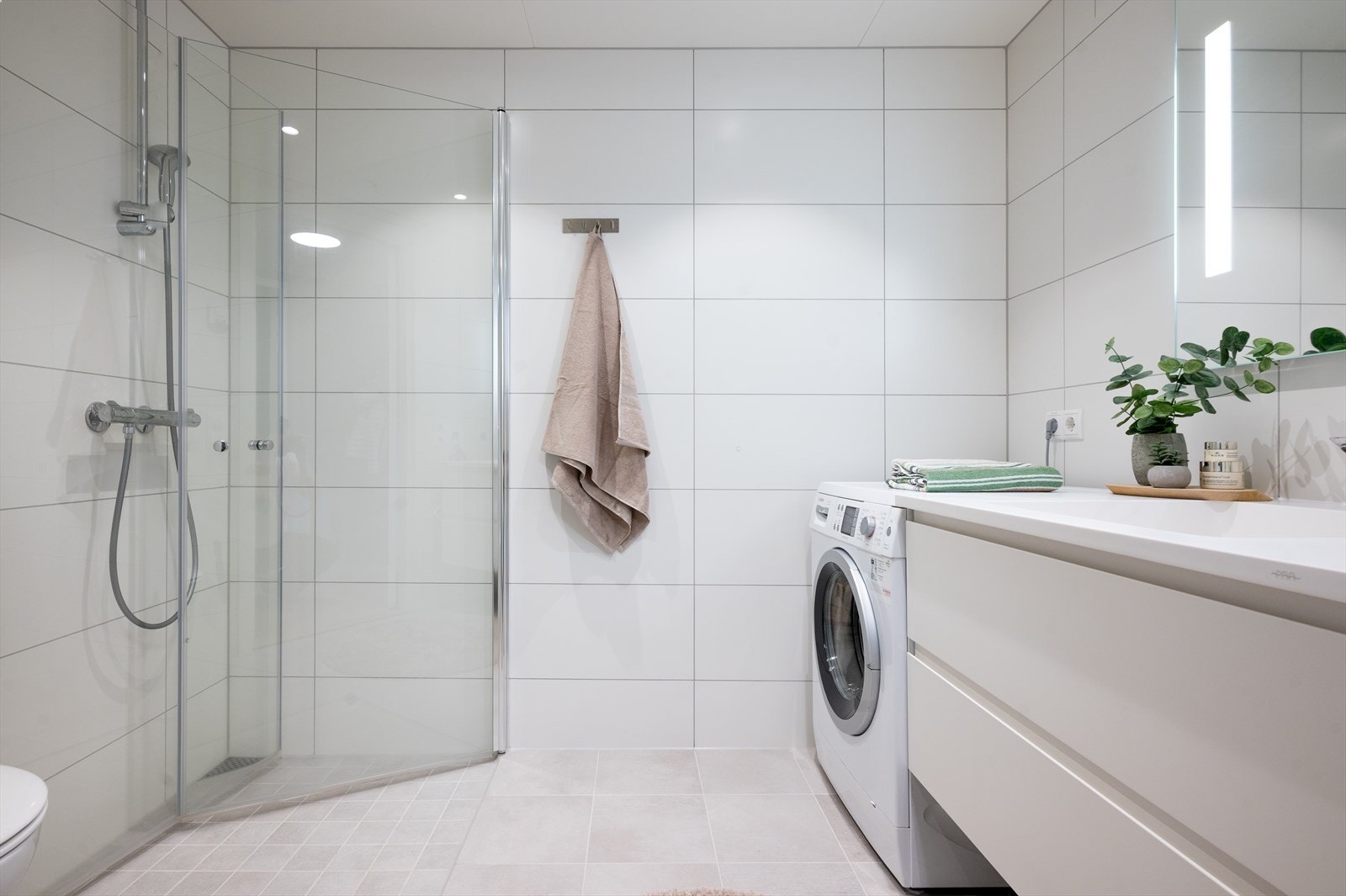 Flislagt baderom på 4 kvm. Badet er utstyrt med vegghengt klosett, dusjhjørne med foldbare glassdører, integrerte lys i speil og downlights i himling. Galleribilde