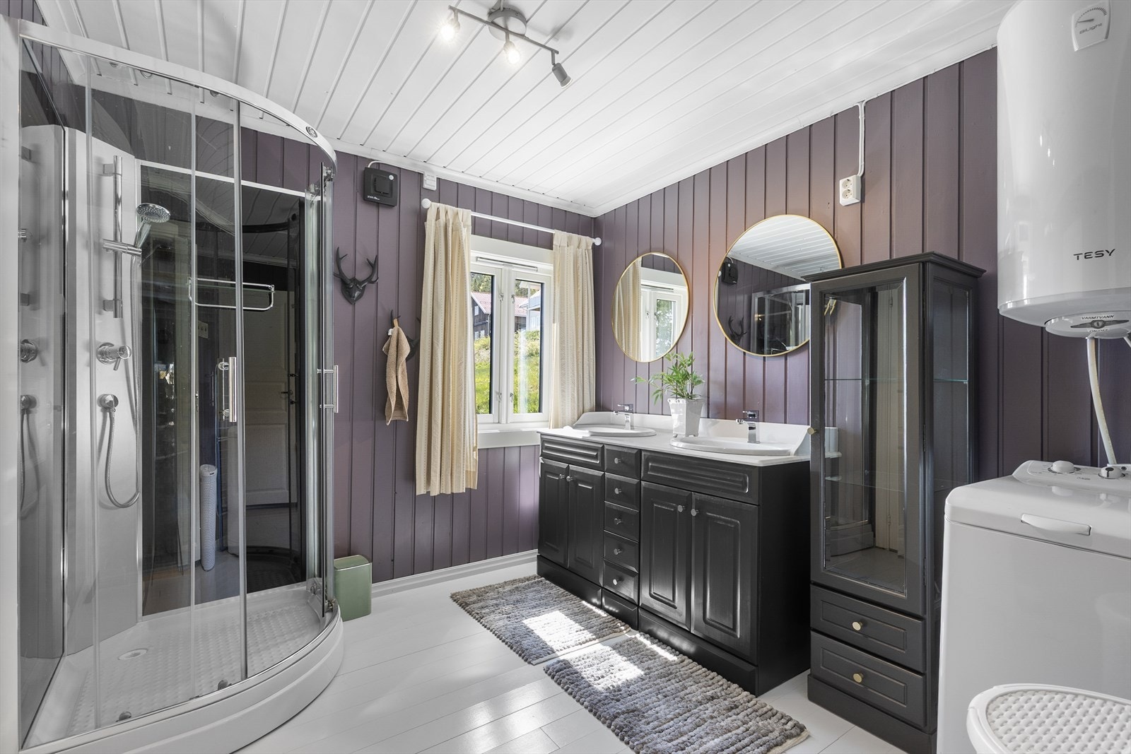 Badet er utstyrt med dusjkabinett, innredning med to servanter og har opplegg for vaskemaskin. Galleribilde