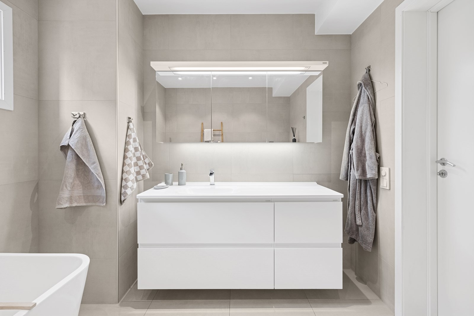 Badet er utstyrt med veggmontert toalett, dusjhjørne med glassvegger, badekar, baderomsinnredning med nedfelt servant, samt speilskap. Galleribilde