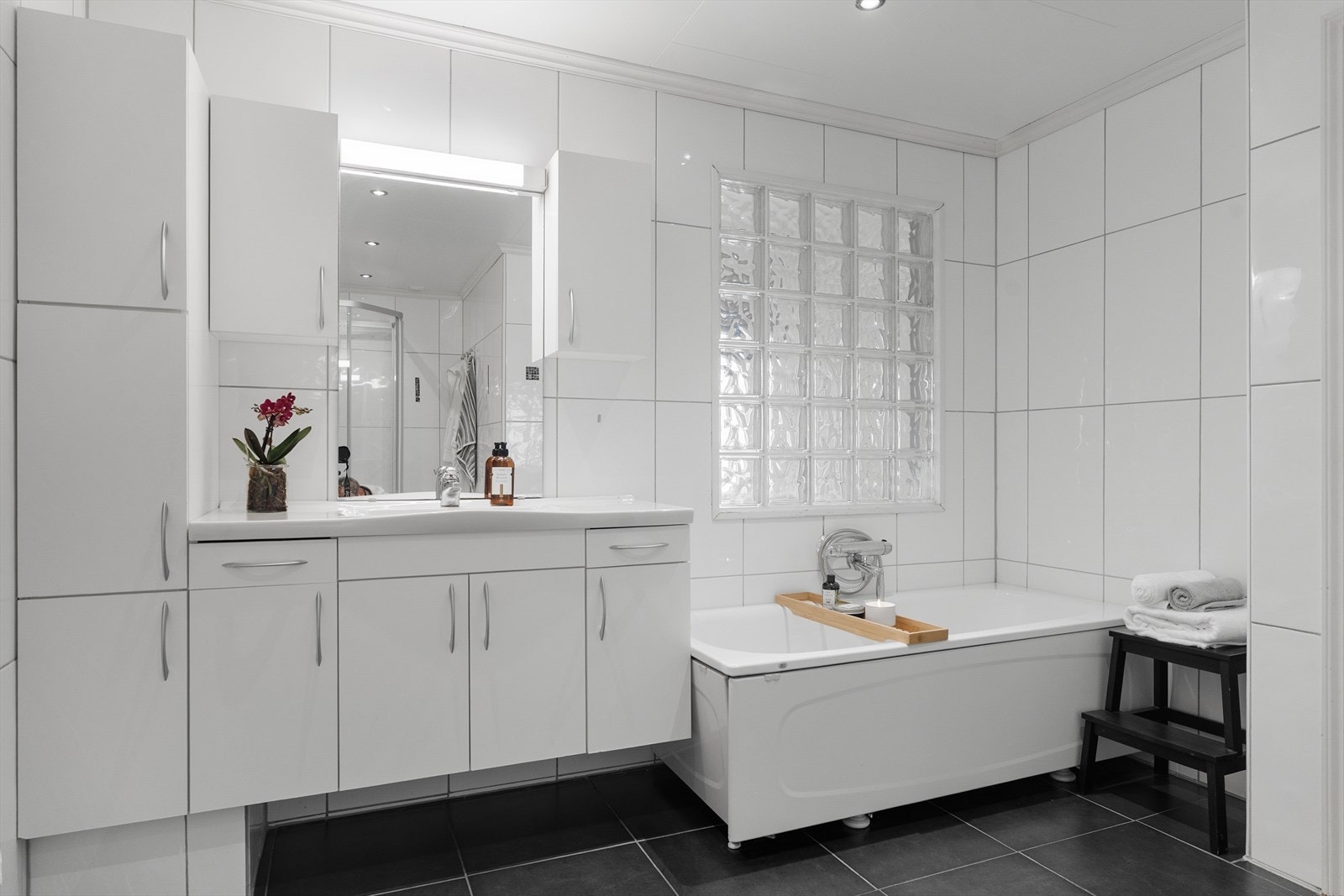 Badet er romslig med vegghengt toalett, badekar, dusjkabinett, hvit baderomsinnredning med skittentøysjakt ned til bad i 1. etasje, sideskap, 2 overskap og speil med belysning Galleribilde
