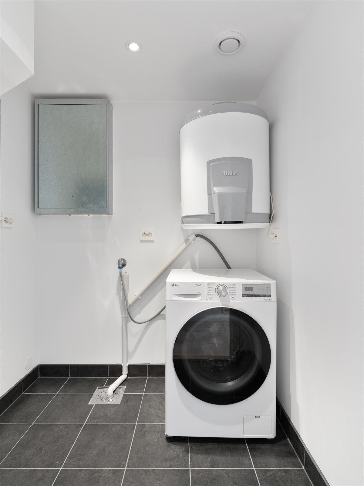 Praktisk vaskerom med flislagt gulv, opplegg for vaskemaskin og plassering av tekniske installasjoner. Galleribilde