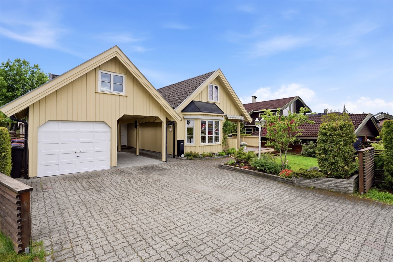 Gårdsplassen har belegningsstein, og parkering i garasje og carport eller på oppstillingsplassen i front. Det er montert elbillader på stolpe i carport. Galleribilde