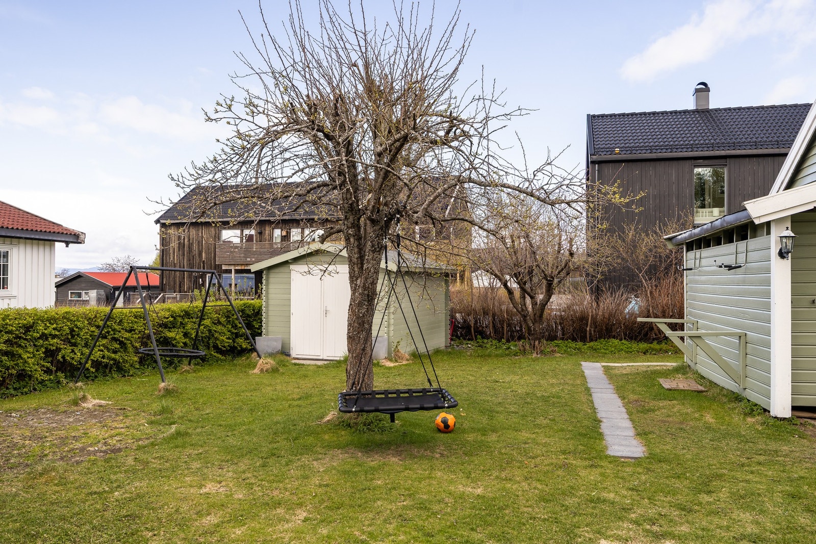 Hage med store grøntarealer og gode solforhold innrammet av busker, perfekt for en barnefamilie. Utebod oppsatt i 2021. Galleribilde