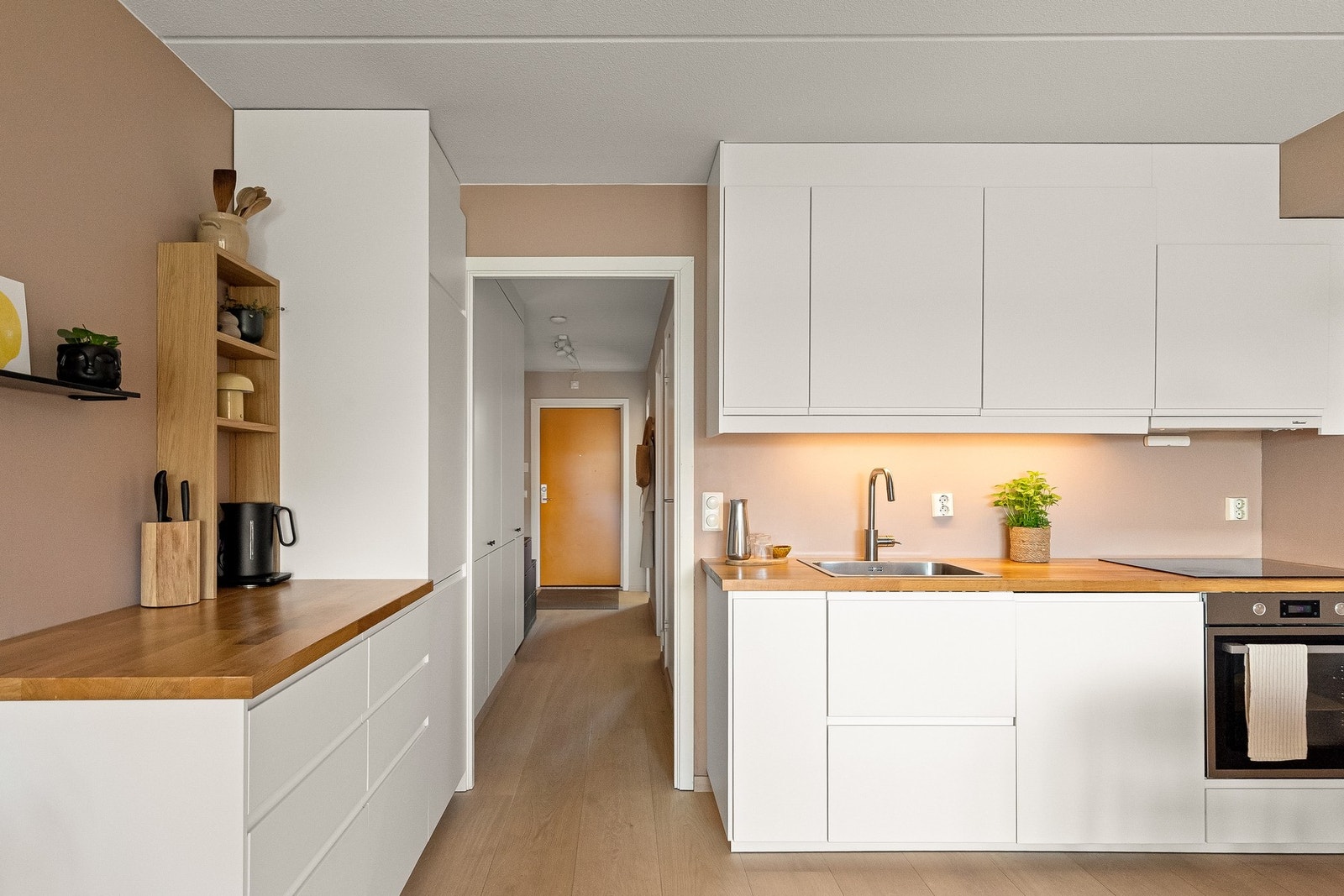Kjøkkeninnredningen er utstyrt med hvite glatte fronter, benkeplate i sponkjerne med nedfelt kum i rustfritt stål og belysning under overskap. Galleribilde