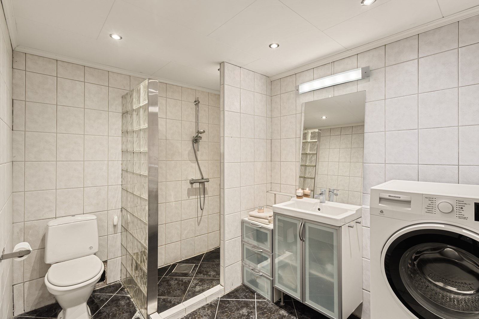 Badet er av god størrelse og inneholder servant med møblement/speil, belysning, toalett, dusjhjørne, dusjgarnityr og opplegg for vaskemaskin. Galleribilde