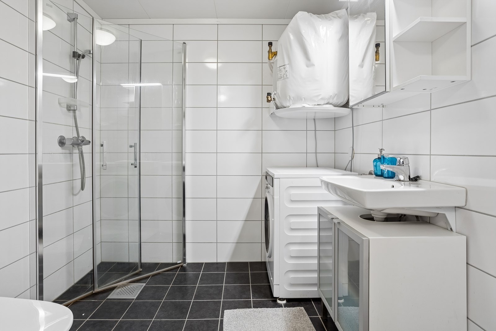 Flislagt bad med gulvvarme. Her er det vendbare dusjdører i glass og opplegg for vaskemaskin. Galleribilde