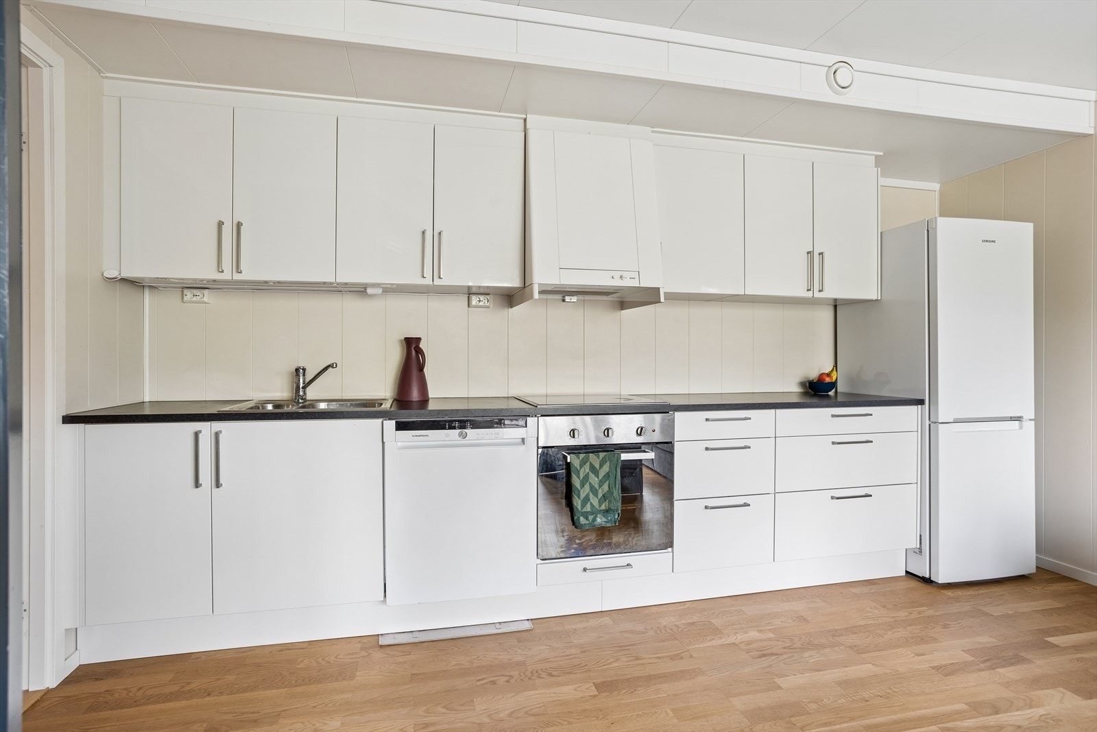 Kjøkkeninnredning med laminatbenkeplate, over- og underskap. Integrert stekeovn og platetopp. Opplegg for oppvaskmaskin. Plass til kjøl/frys. Galleribilde