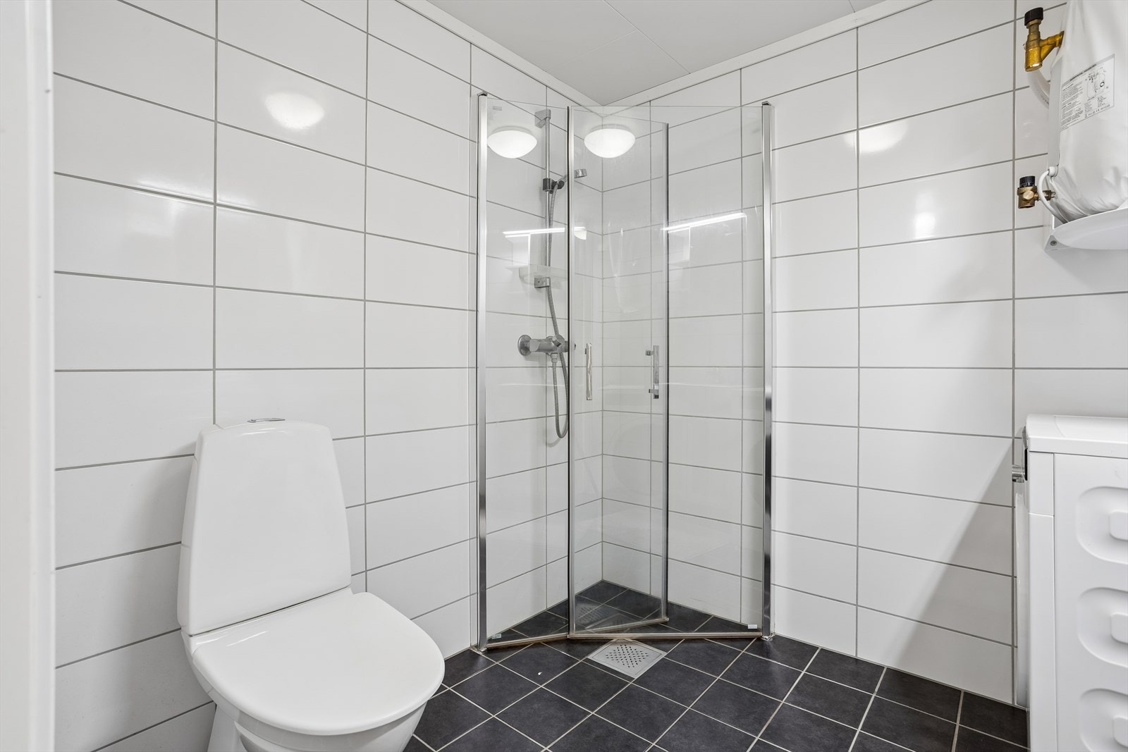 Badet er er utstyrt med toalett, servant med underskap og speilskap, samt dusjhjørne. Galleribilde