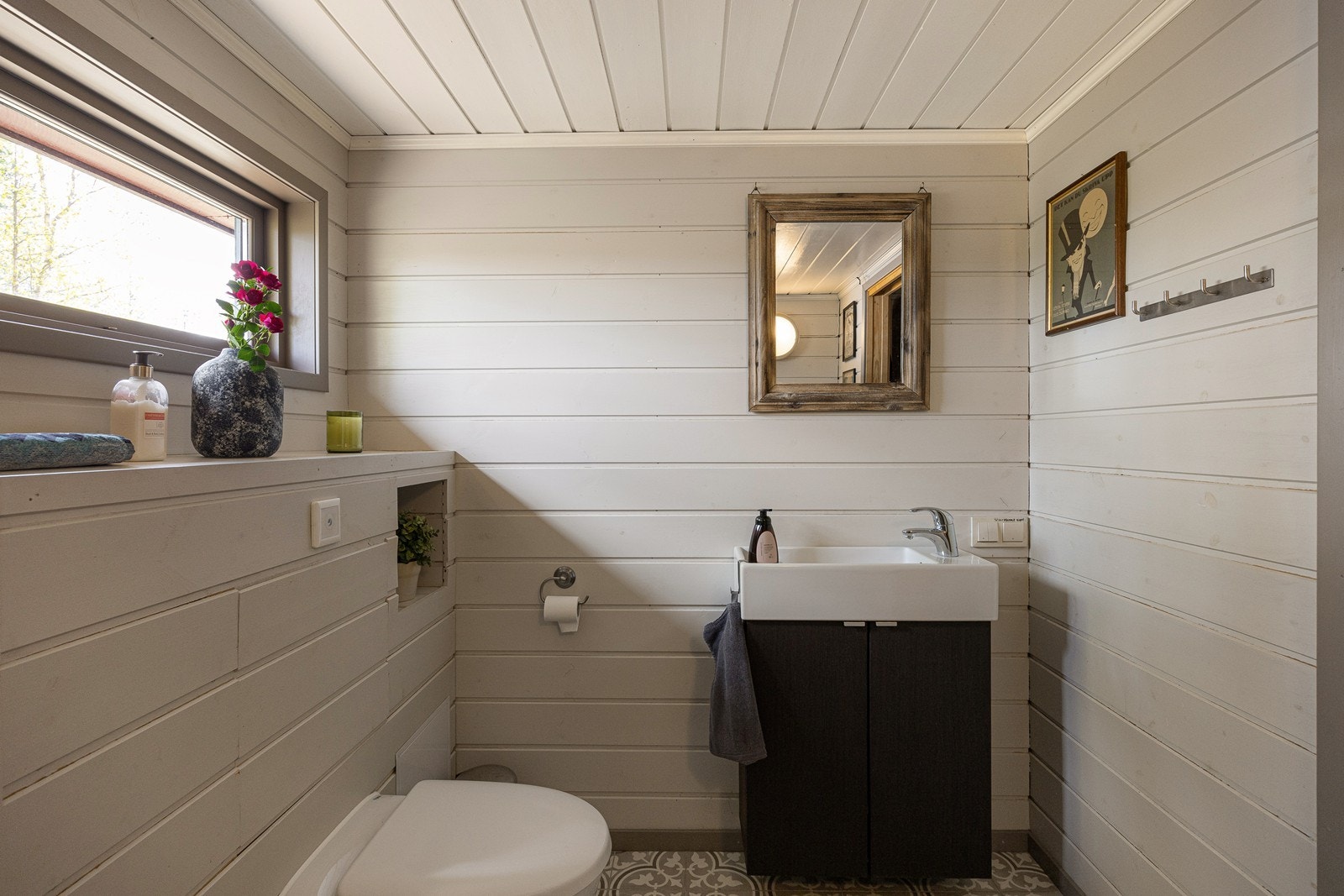 Badet ble pusset opp i 2014 og fremstår som funksjonelt og pent. Rommet er utført med gråmalte vegger og tak i panel, kombinert med nostalgiske mønsterfliser på gulv med gulvvarme. Galleribilde