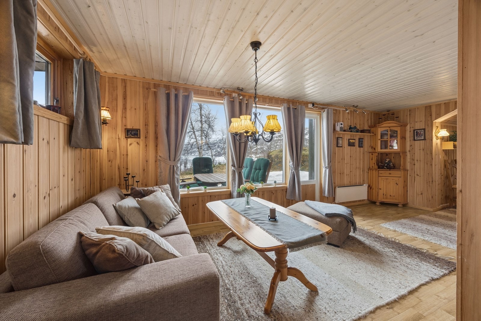Stuen har panel på vegger og i tak, og vinduer som rammer inn utsikten mot naturen. Galleribilde