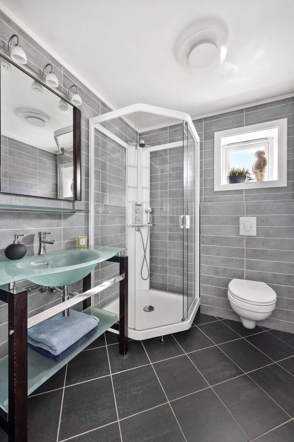 Badet i 2. etasje har et moderne og stilrent uttrykk med helflisede overflater i grå toner som skaper en tidløs og harmonisk atmosfære. Galleribilde