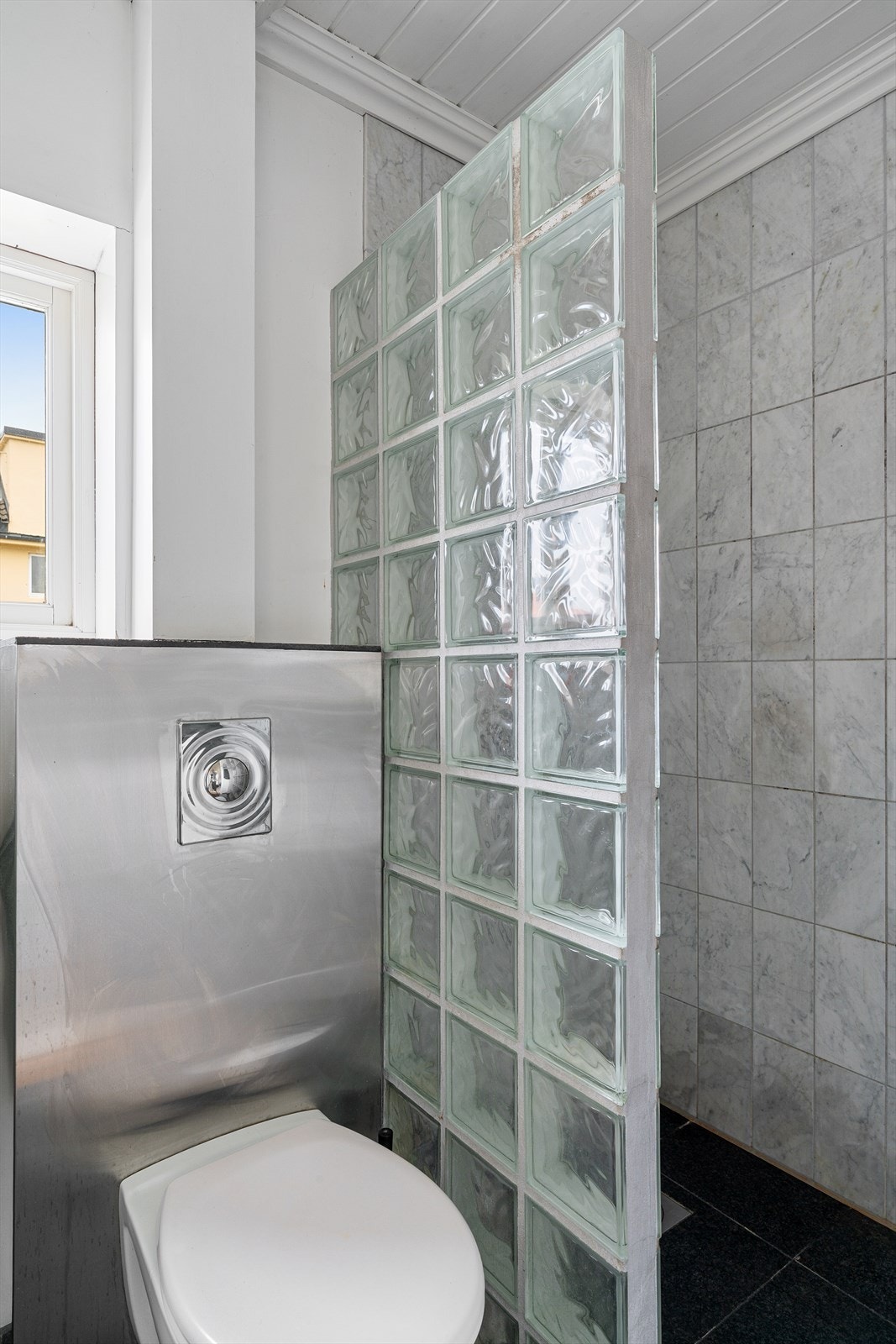 Badet er innredet med servant, vegghengt toalett og dusjhjørne med fliser på vegg. Galleribilde