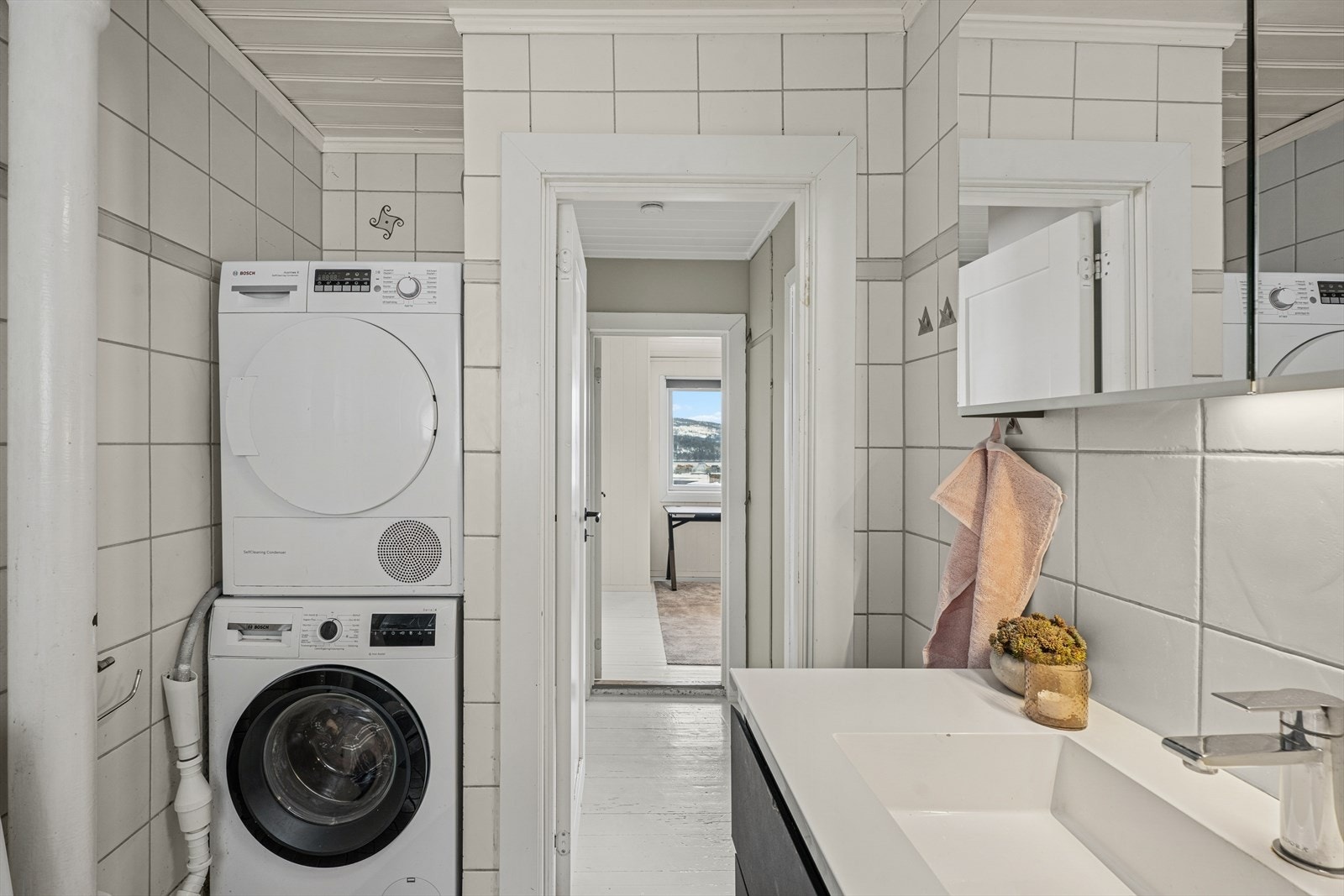 Badet har flislagte vegger med hvite fliser, grå fuger og en dekorativ grå bård, samt flislagt gulv med termostatstyrt gulvvarme Galleribilde
