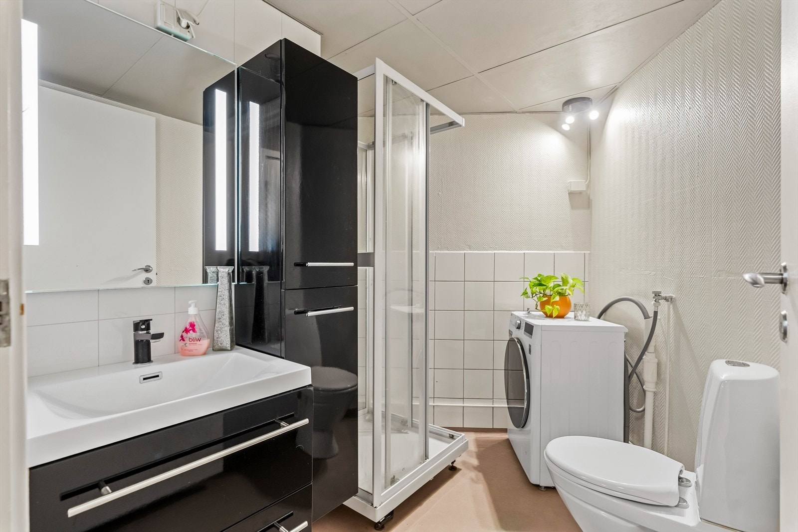 Badet er innredet med toalett, dusjkabinett, servant, veggskap, speil med belysning og opplegg for vaskemaskin. Galleribilde