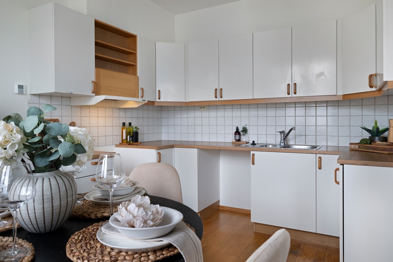 Kjøkkenet har innredning med glatte fronter. Benkeplaten er av laminat, fliser på vegg over kjøkkenbenk. Det er parkett på gulv. Det er kjøkkenventilator med avtrekk ut. Galleribilde