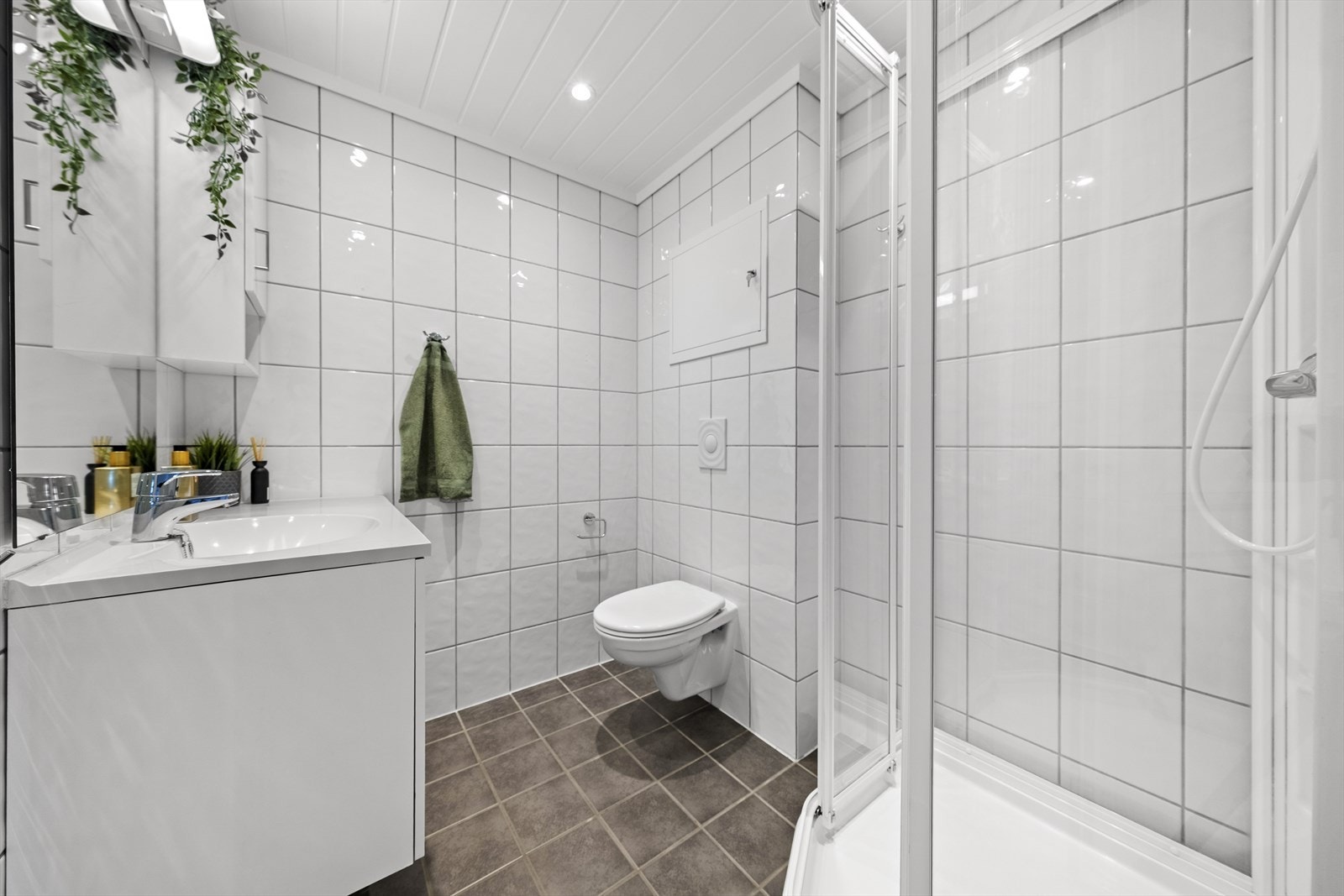 Pent helfliset baderom med varmekabler i gulv. Badet er utstyrt med servant over innredning, speil med overliggende belysning, sideskap, vegghengt toalett og dusjkabinett Galleribilde