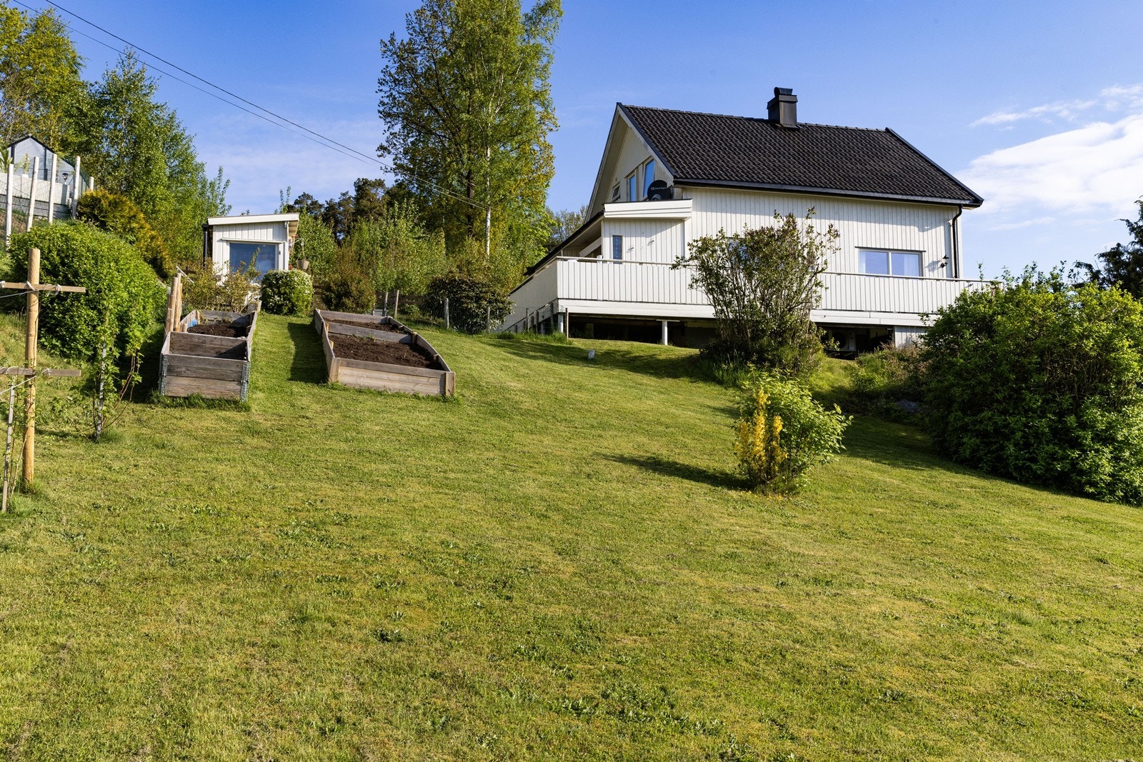 Den skrånende tomten er pent opparbeidet med plen og plantekasser, og ligger i et område som oppleves som svært trygt med lite trafikk. Galleribilde
