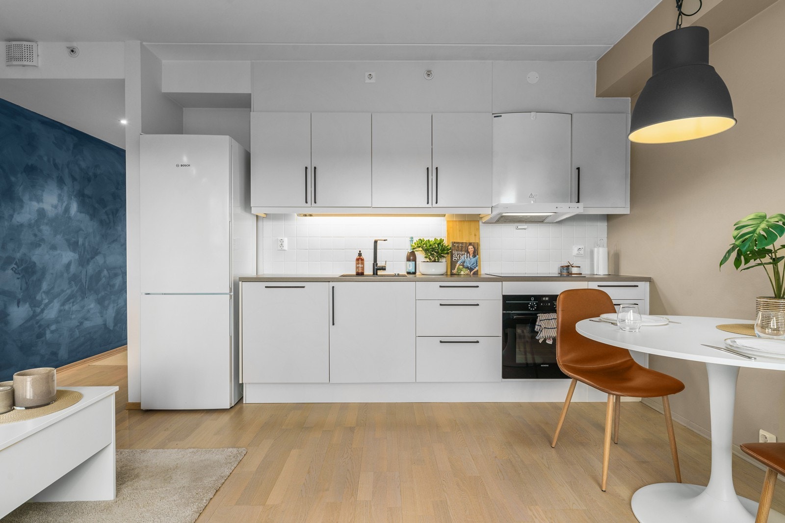 Kjøkkeninnredning med glatte, hvite fronter og integrert stekeovn, koketopp og oppvaskmaskin. Galleribilde