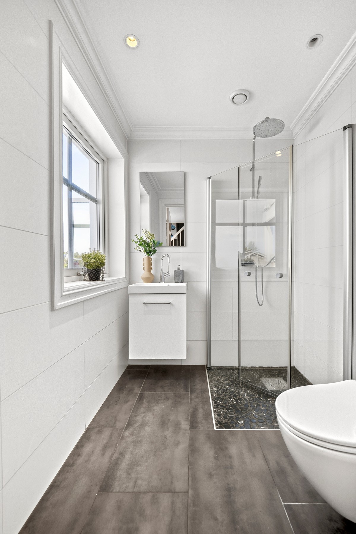 Badet i første etasje har vindu mot terrassen, veggmontert toalett, hvit servantinnredning og regnfallsdusj. Galleribilde