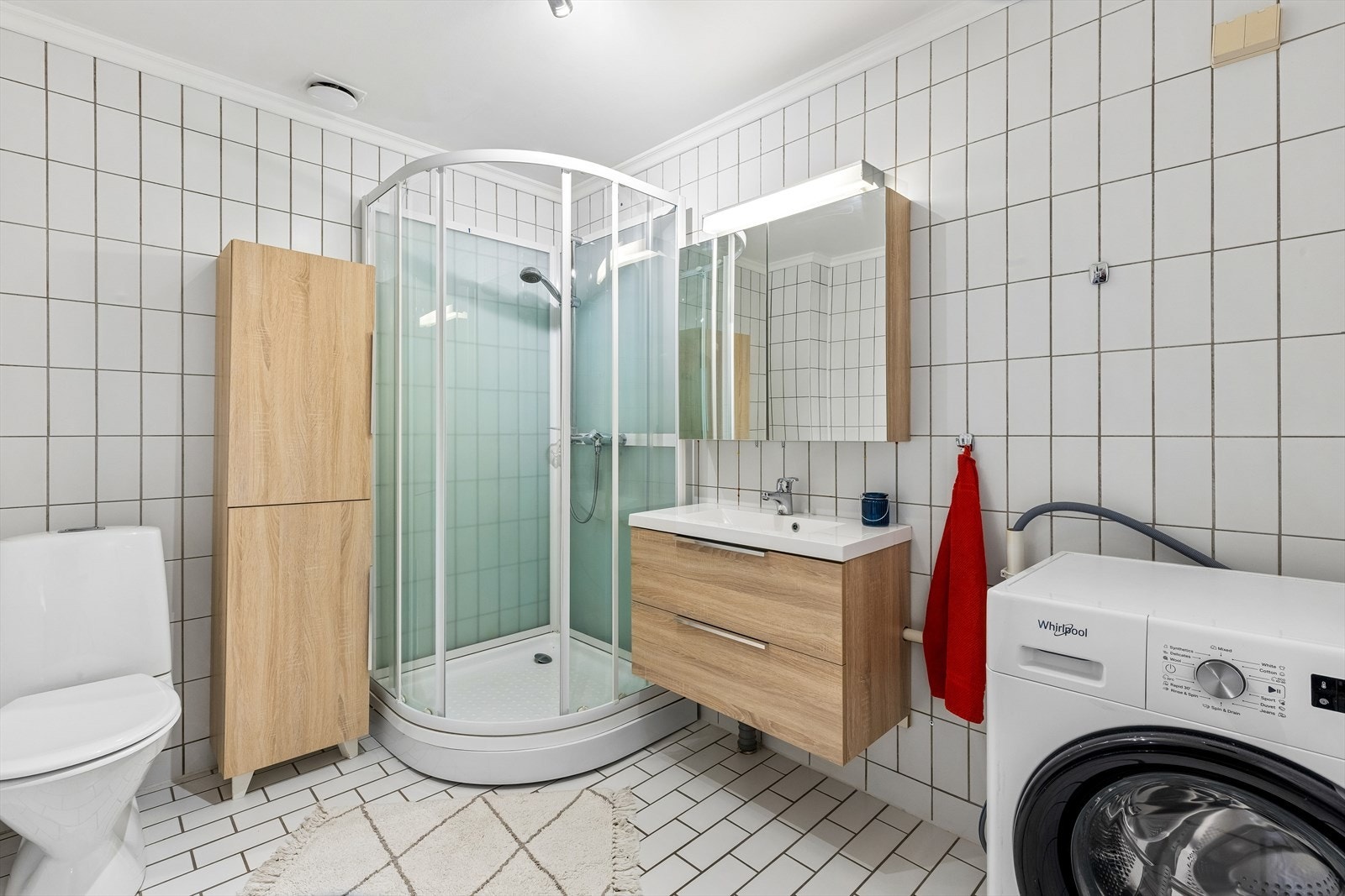 Badet er flislagt og utstyrt med dusjkabinett, servantskap og opplegg for vaskemaskin. Galleribilde