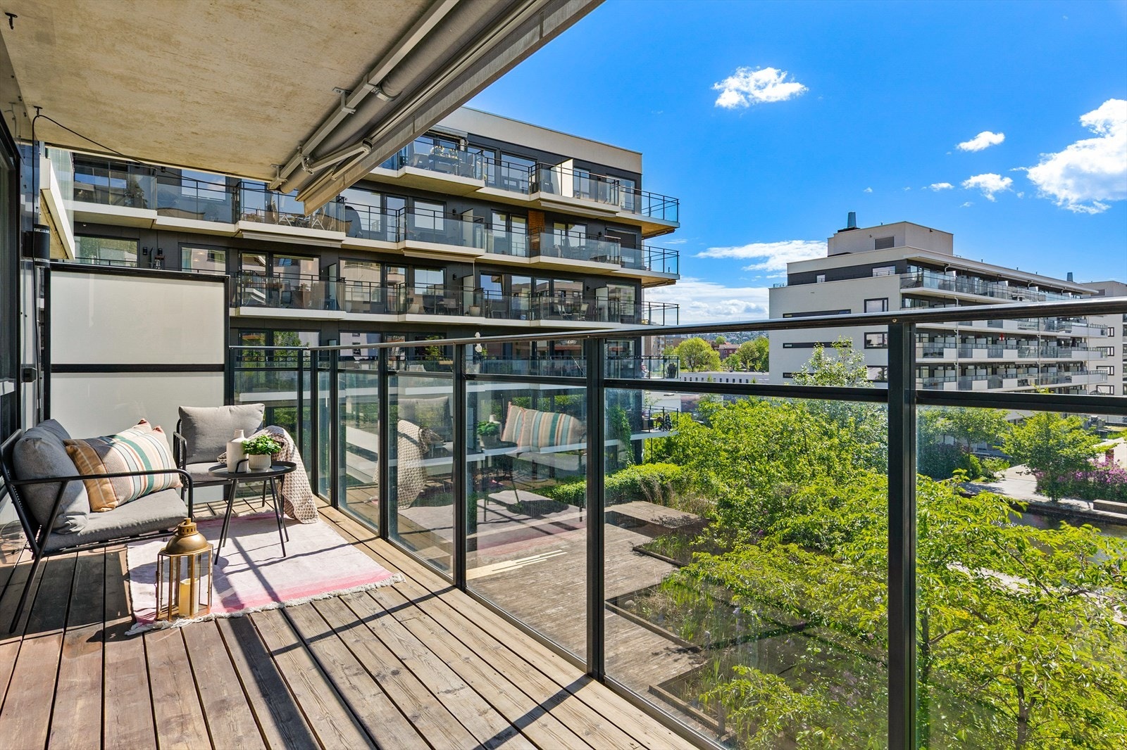 Balkongen har terrassebord, rekkverk i lakkert stål og glass, og utsikt mot de pent opparbeidede fellesområdene Galleribilde