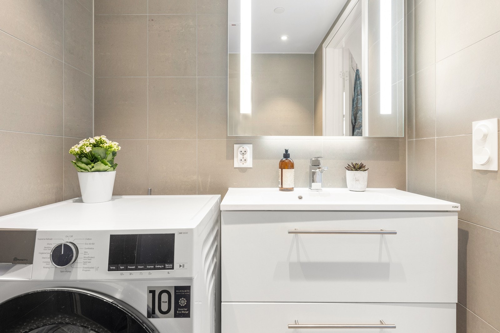 Badet er utstyrt med vegghengt toalett, servantskap, speil på vegg, dusjhjørne med glassdører og ettgreps dusjarmatur fra Grohe. Det er også opplegg for vaskemaskin. Galleribilde